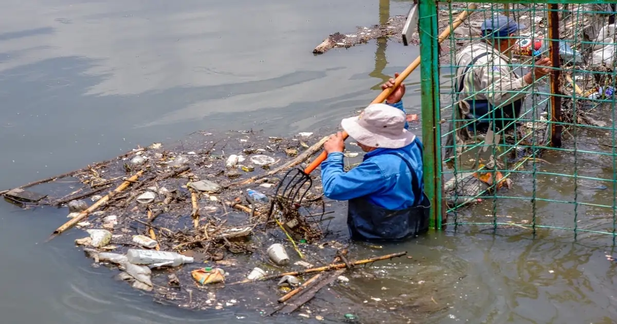 Workers removing plastic waste from a polluted waterbody to reduce environmental damage.