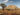 Arid desert landscape with scattered drought-resistant plants and sandy soil under a clear sky.