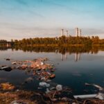 An image depicting industrial waste, plastic debris, and agricultural runoff contaminating a water body.