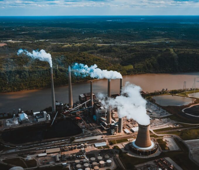 Industrial facility releasing emissions near water and land, highlighting major causes of environmental pollution