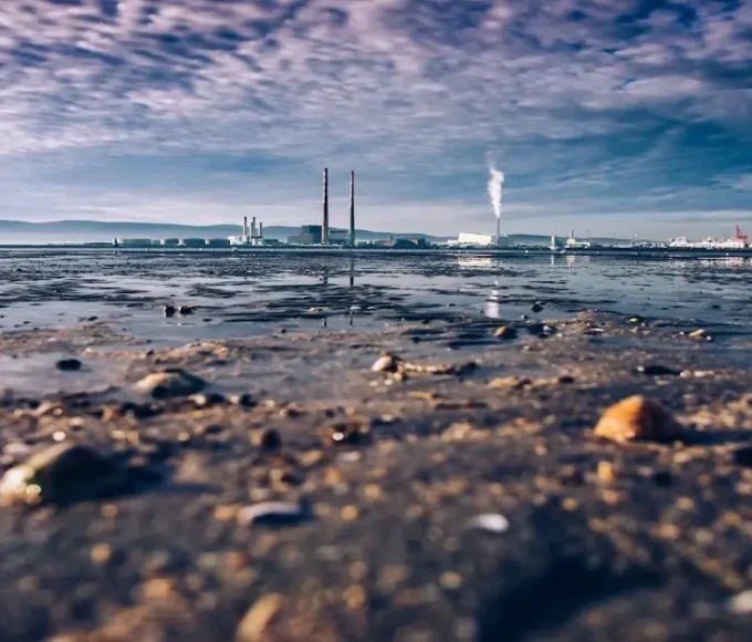 Industrial emissions near a coastline showing air and water pollution impacts on the natural environment